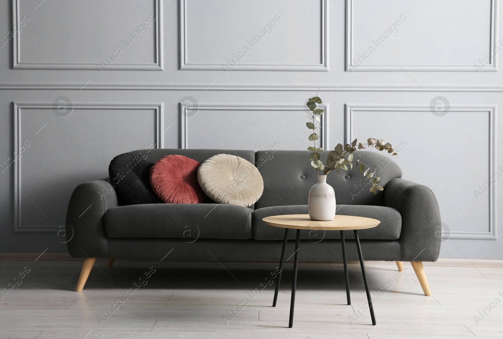 Photo of Stylish sofa with cushions and eucalyptus branches in vase on coffee table in room