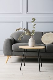 Stylish sofa with cushion and eucalyptus branches in vase on coffee table in room