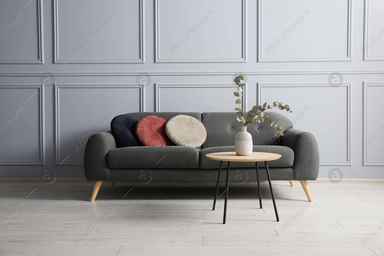 Photo of Stylish sofa with cushions and eucalyptus branches in vase on coffee table in room