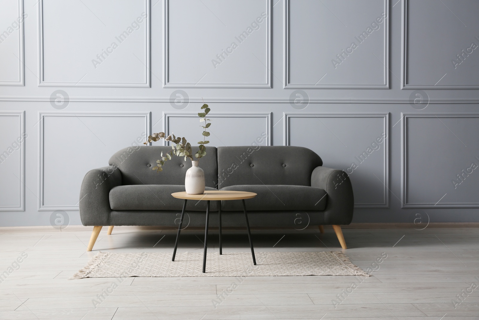 Photo of Stylish sofa and eucalyptus branches in vase on coffee table in room