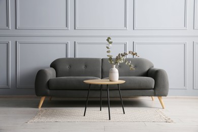 Photo of Stylish sofa and eucalyptus branches in vase on coffee table in room