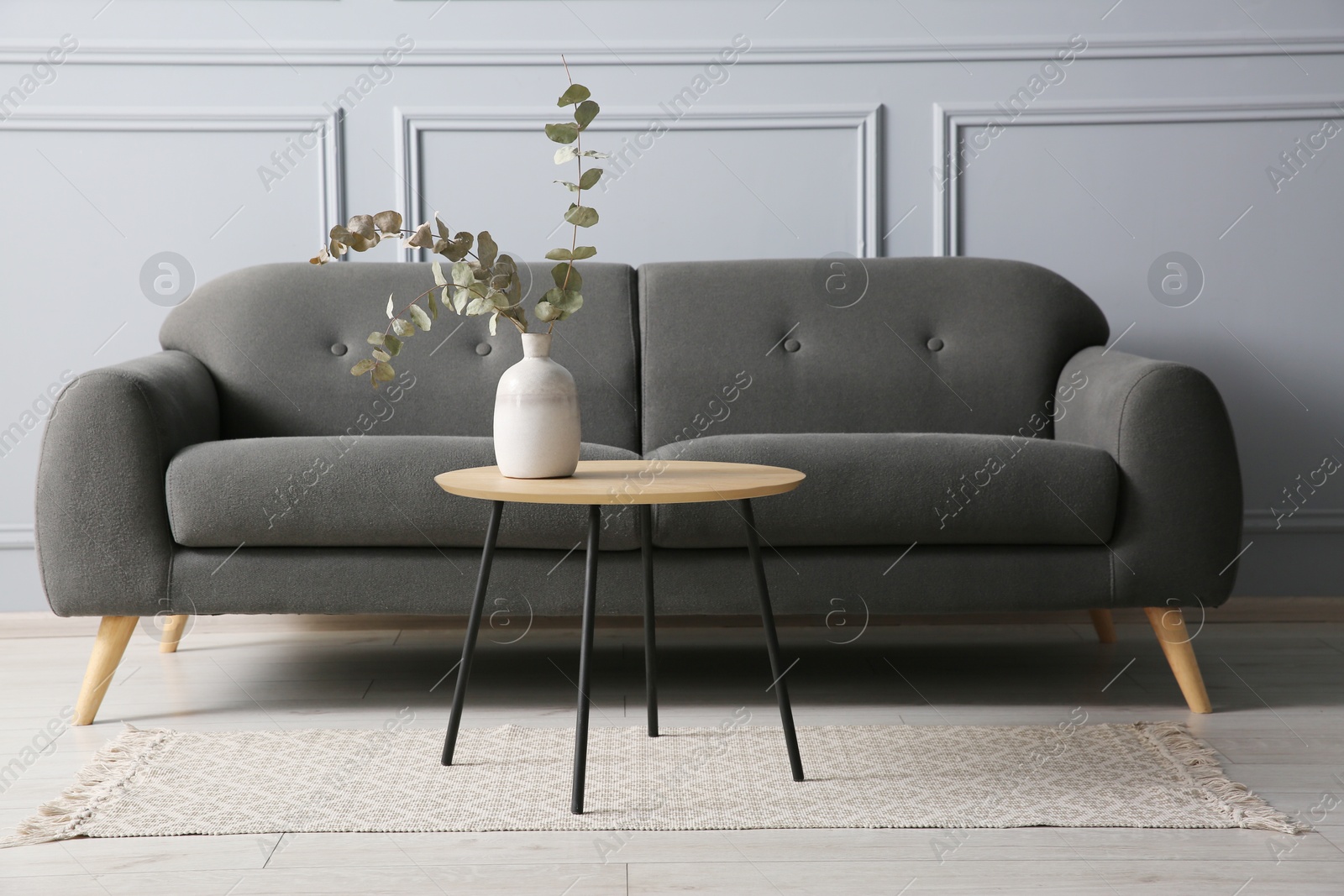 Photo of Stylish sofa and eucalyptus branches in vase on coffee table in room