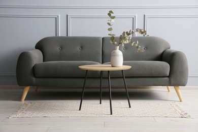 Photo of Stylish sofa and eucalyptus branches in vase on coffee table in room