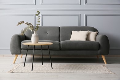 Stylish sofa with cushions and eucalyptus branches in vase on coffee table in room