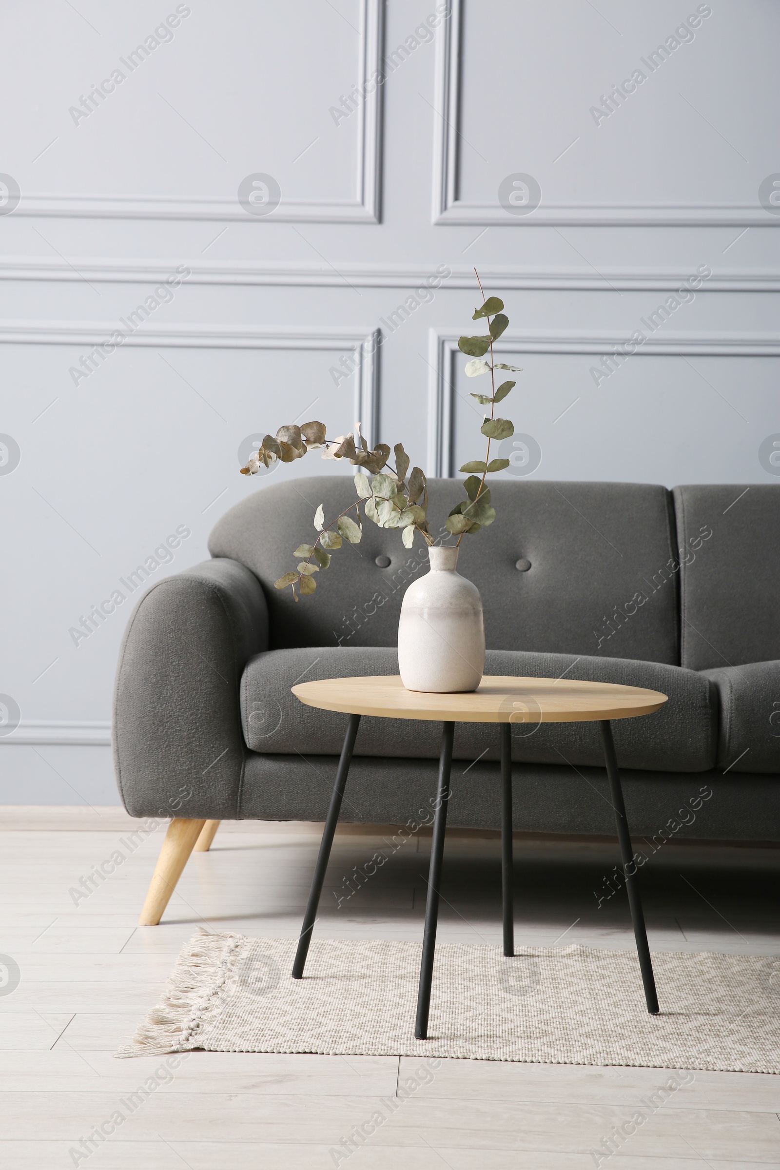 Photo of Stylish sofa and eucalyptus branches in vase on coffee table in room