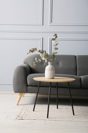 Stylish sofa and eucalyptus branches in vase on coffee table in room