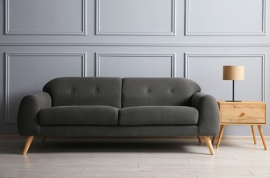 Photo of Stylish sofa and lamp on side table near grey wall