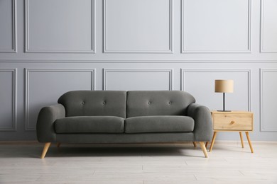 Stylish sofa and lamp on side table near grey wall