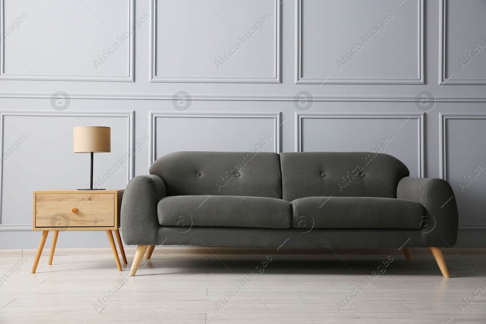 Photo of Stylish sofa and lamp on side table near grey wall