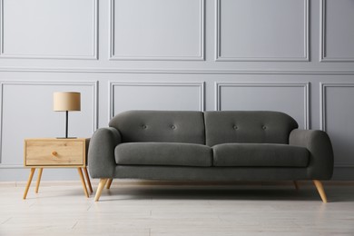 Photo of Stylish sofa and lamp on side table near grey wall