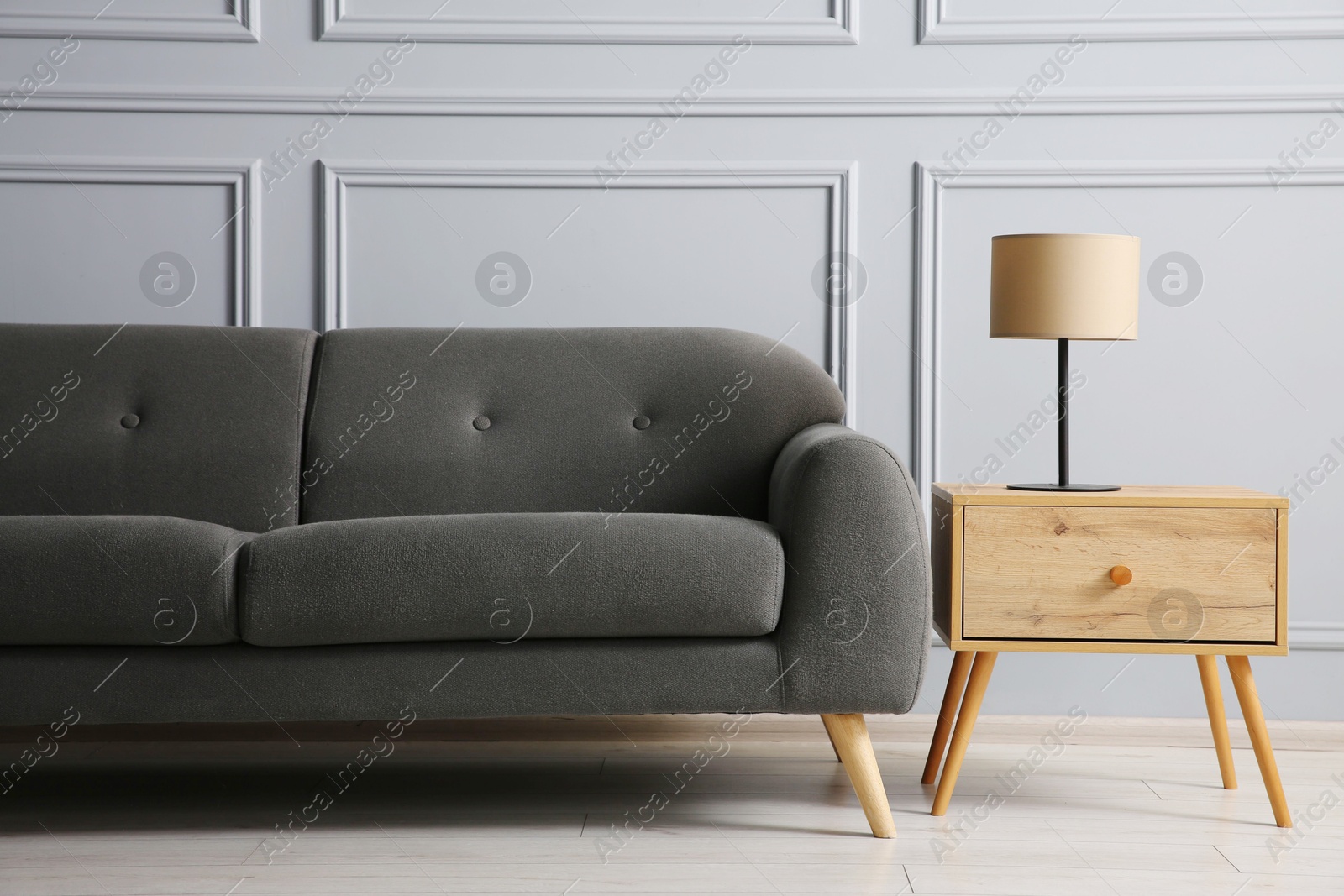 Photo of Stylish sofa and lamp on side table near grey wall