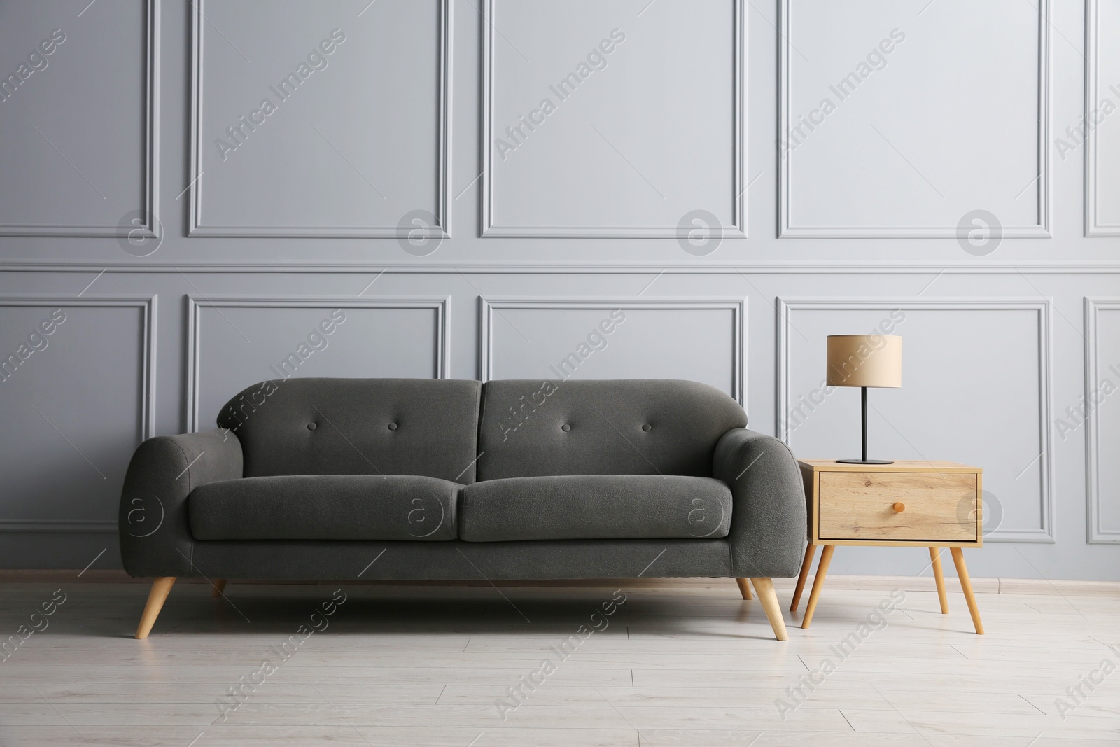 Photo of Stylish sofa and lamp on side table near grey wall