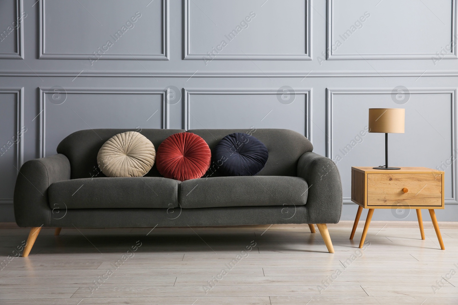 Photo of Stylish sofa with cushions and lamp on side table near grey wall