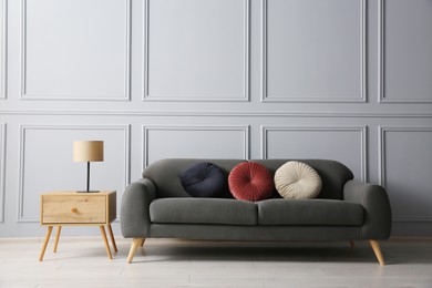 Stylish sofa with cushions and lamp on side table near grey wall