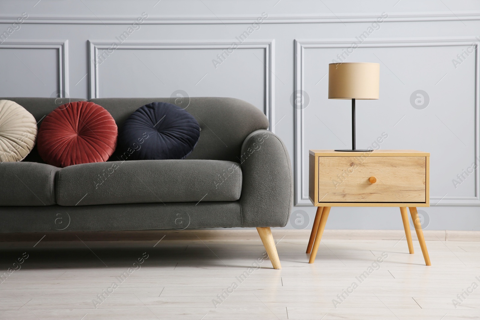 Photo of Stylish sofa with cushions and lamp on side table near grey wall