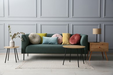 Stylish sofa with cushions, lamp and eucalyptus branches on side tables in room