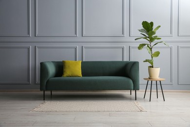 Photo of Stylish sofa with cushion and green plant near on side table grey wall