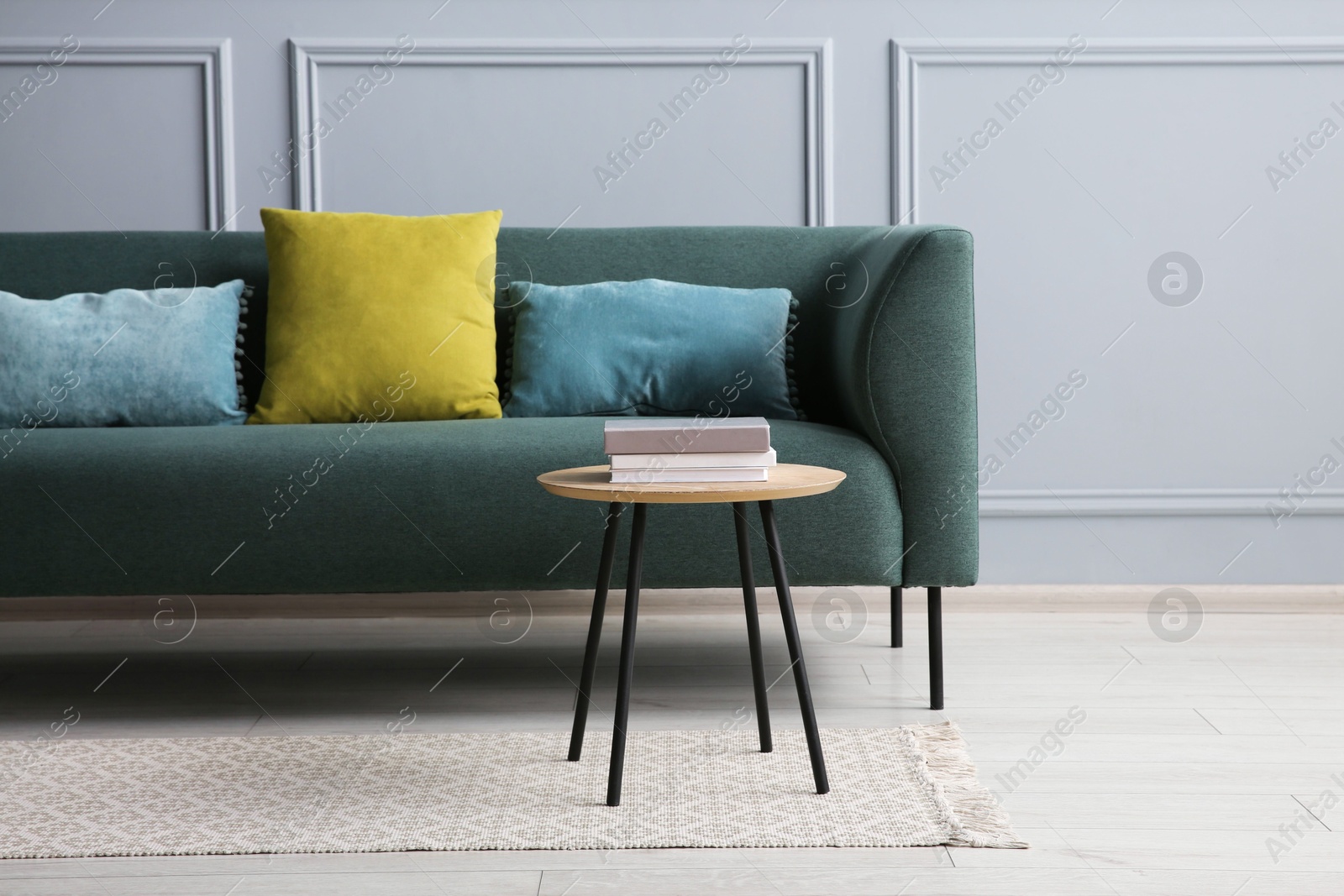 Photo of Stylish sofa with cushions and books on coffee table in room