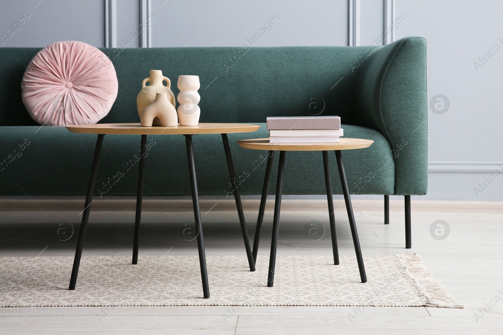 Photo of Stylish sofa with cushion, books and decor elements on nesting tables in room