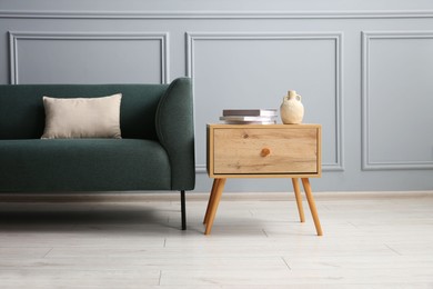 Photo of Stylish sofa with cushion and books on side table near grey wall