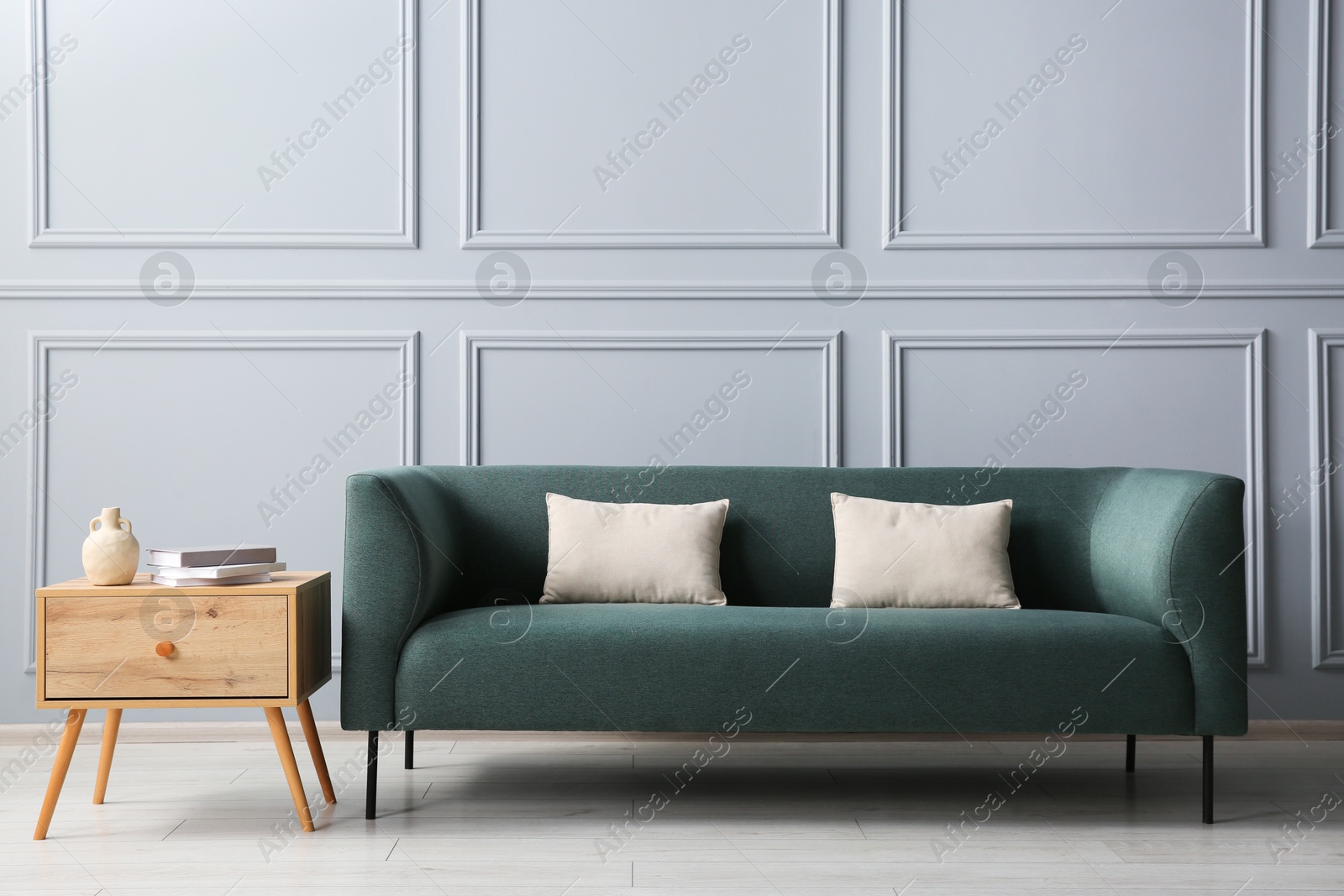 Photo of Stylish sofa with cushions and books on side table near grey wall