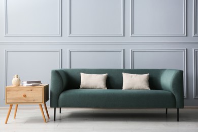 Photo of Stylish sofa with cushions and books on side table near grey wall