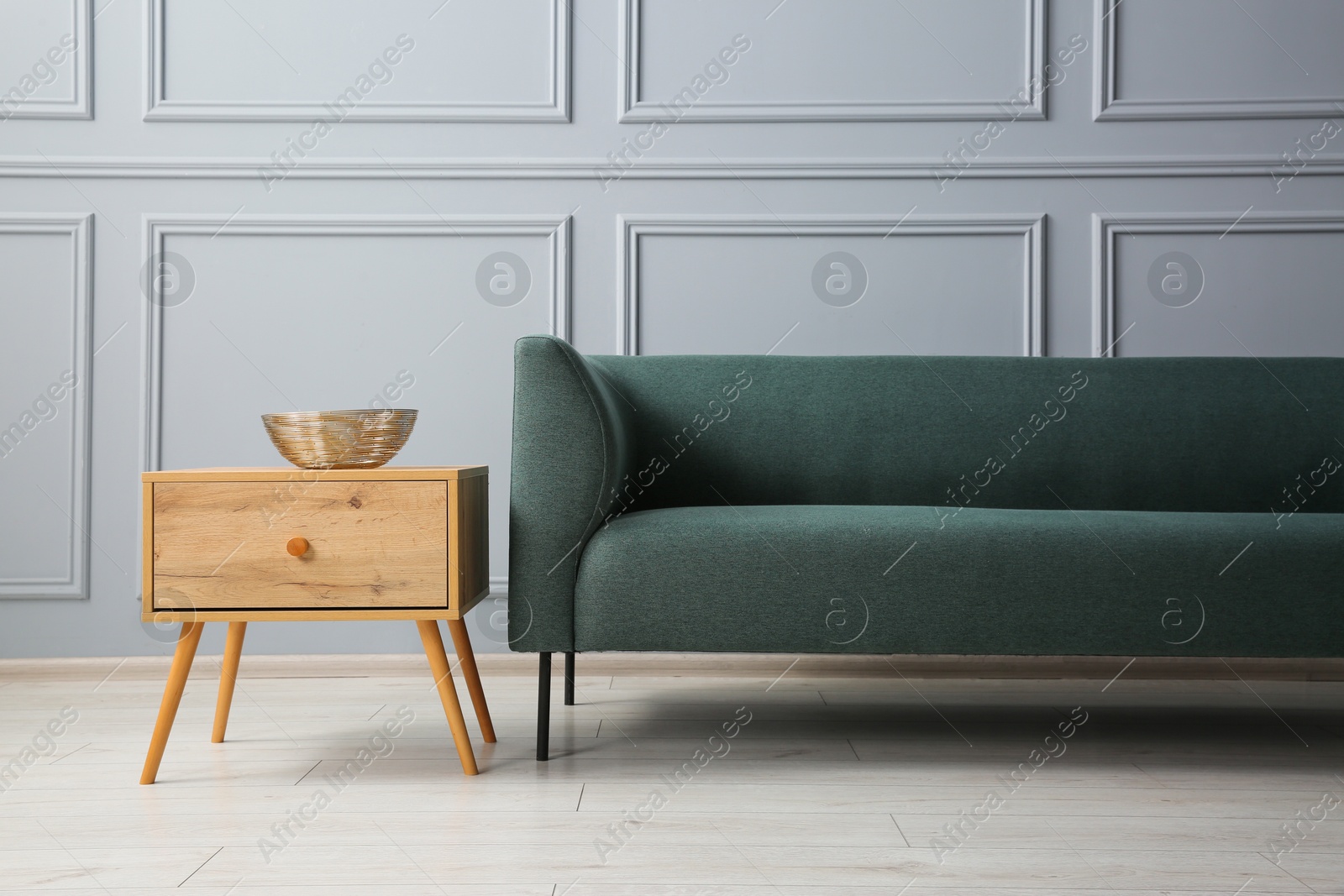 Photo of Stylish sofa and bowl on side table near grey wall