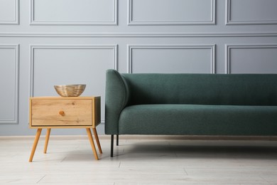 Photo of Stylish sofa and bowl on side table near grey wall