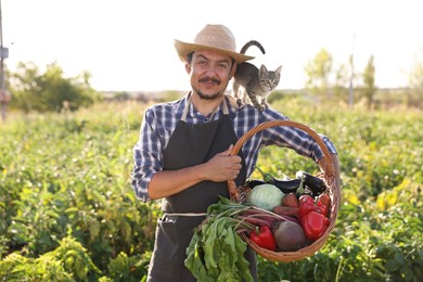 Photo of Harvesting season. Farmer holding wicker basket with fresh vegetables in field on sunny day