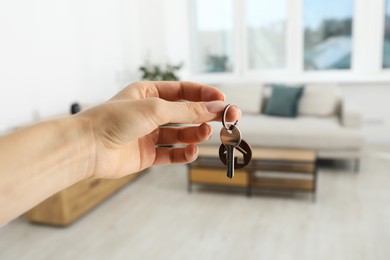 Photo of Woman holding key with house shaped keychain indoors, closeup