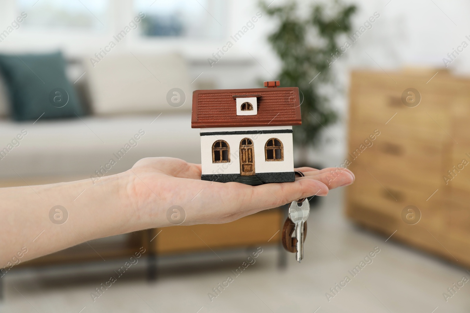 Photo of Woman holding key with keychain and house model indoors, closeup