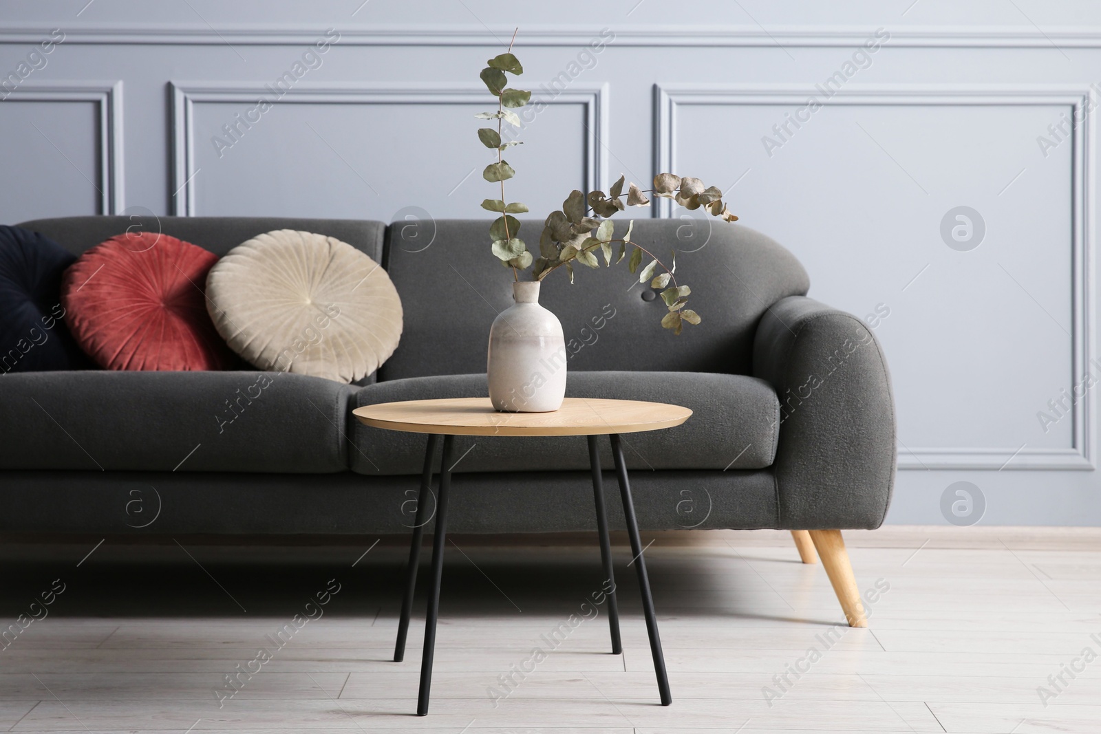 Photo of Stylish sofa with cushions and eucalyptus branches in vase on coffee table in room