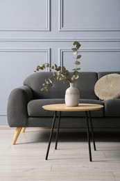 Photo of Stylish sofa with cushion and eucalyptus branches in vase on coffee table in room