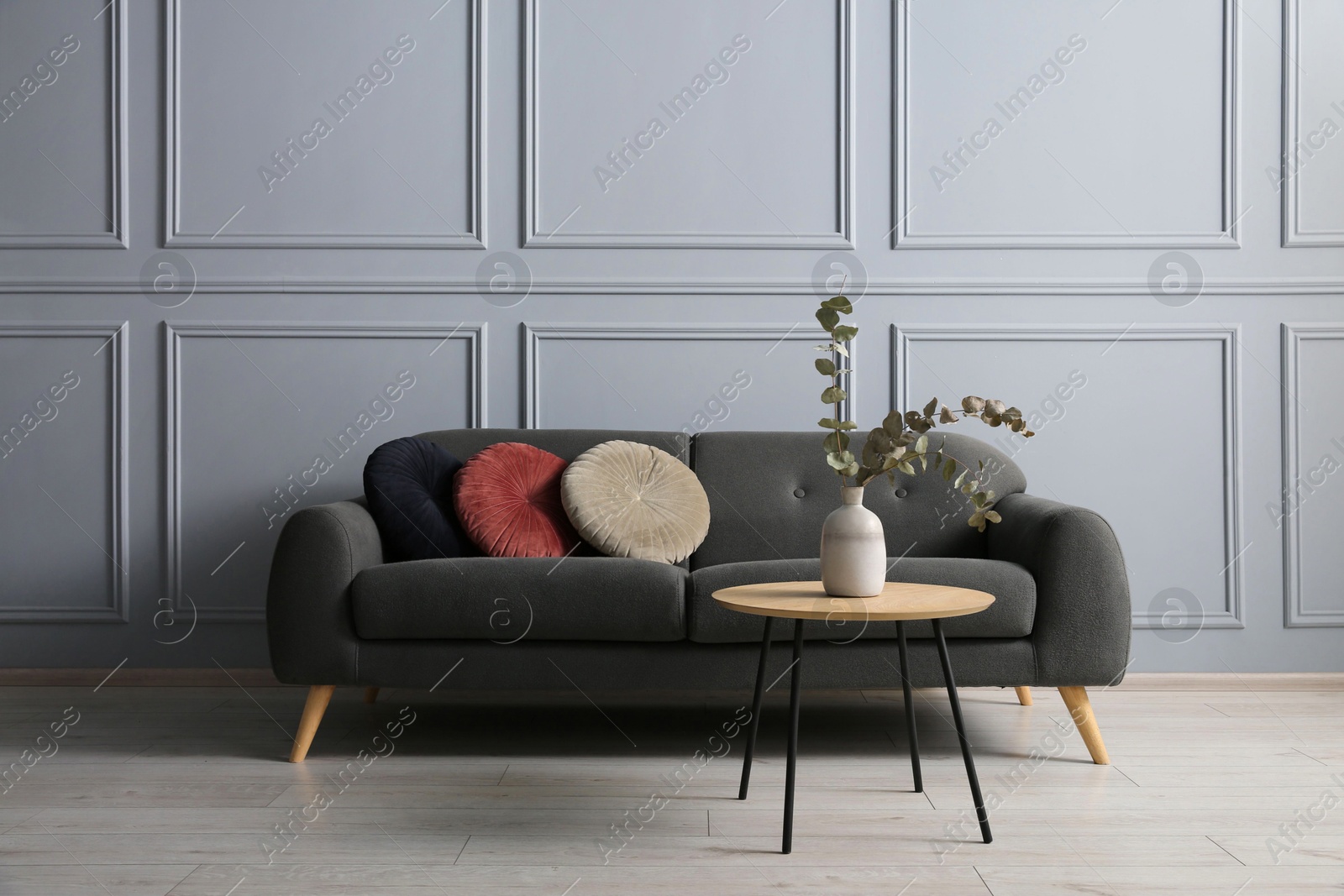 Photo of Stylish sofa with cushions and eucalyptus branches in vase on coffee table in room