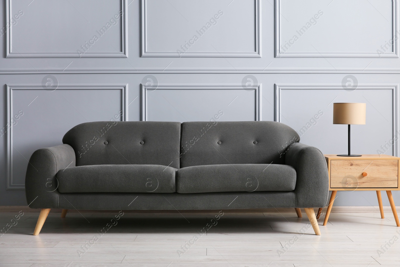 Photo of Stylish sofa and lamp on side table near grey wall