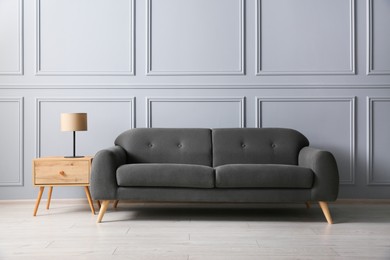 Photo of Stylish sofa and lamp on side table near grey wall