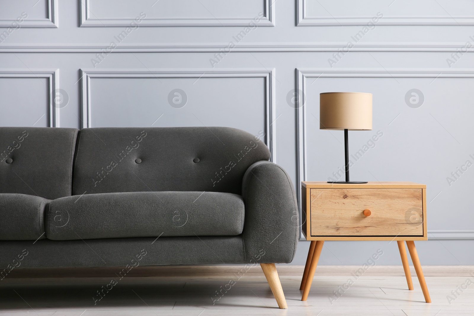 Photo of Stylish sofa and lamp on side table near grey wall