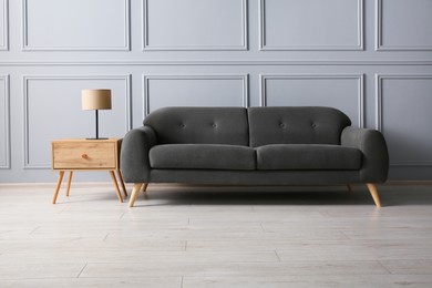 Photo of Stylish sofa and lamp on side table near grey wall