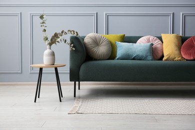 Photo of Stylish sofa with cushions and eucalyptus branches in vase on side table near grey wall