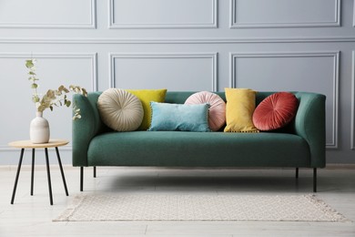 Photo of Stylish sofa with cushions and eucalyptus branches in vase on side table near grey wall