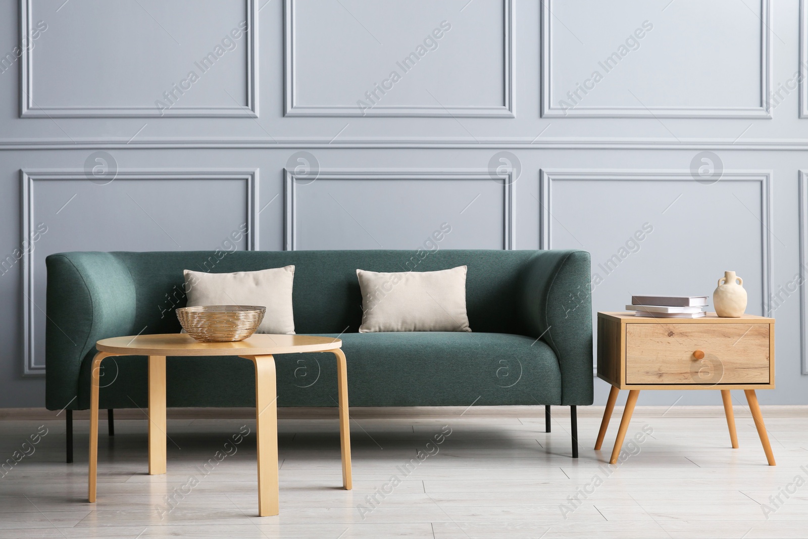 Photo of Stylish sofa with cushions, books and decor elements on side tables in room