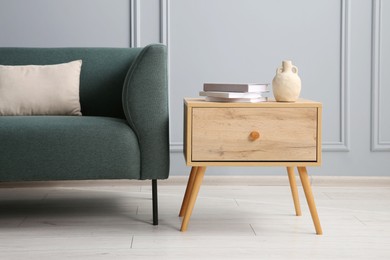 Photo of Stylish sofa with cushion and books on side table near grey wall