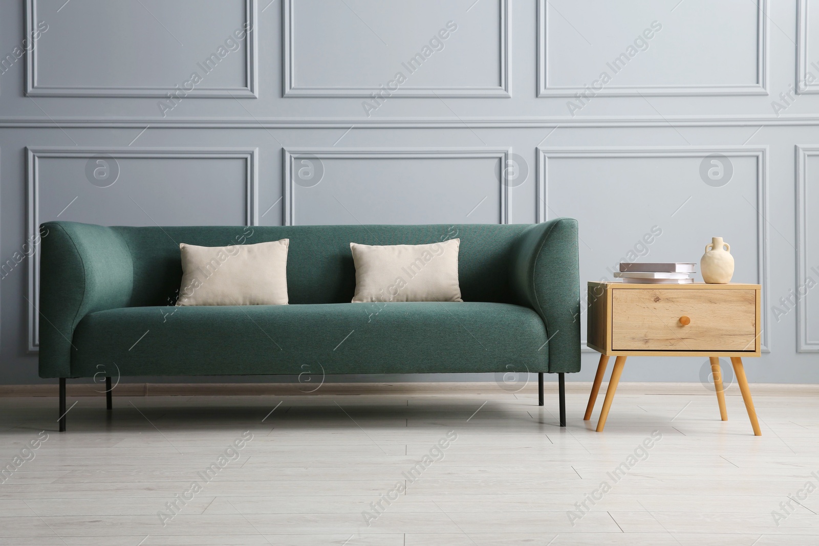 Photo of Stylish sofa with cushions and books on side table near grey wall