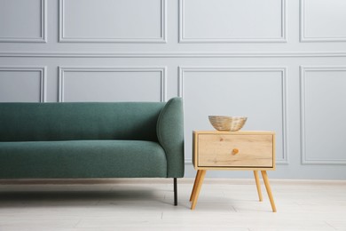 Photo of Stylish sofa and bowl on side table near grey wall