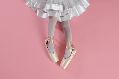 Little ballerina wearing pointe shoes on pink background, top view