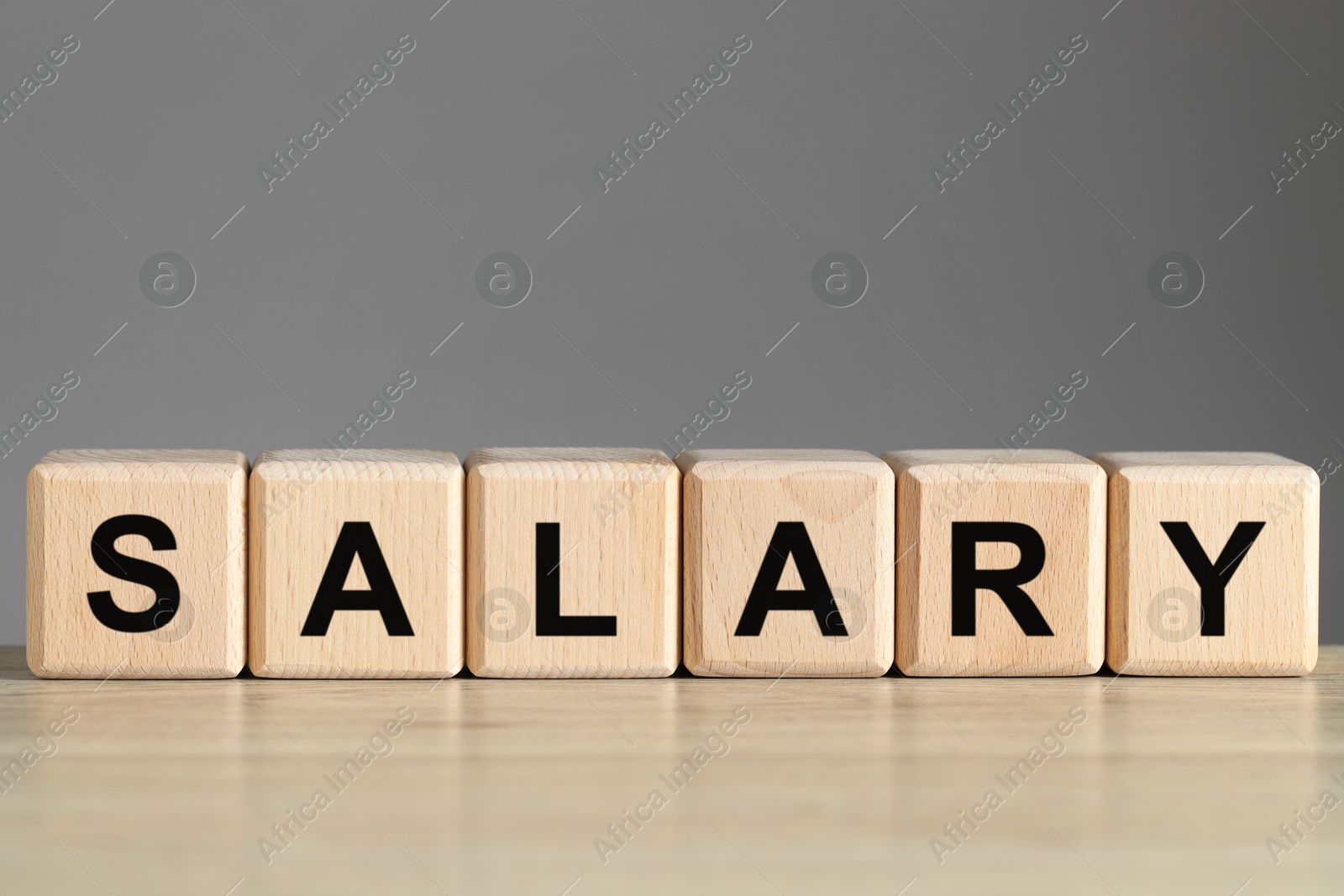 Photo of Word Salary made of cubes on light wooden table against grey background, closeup