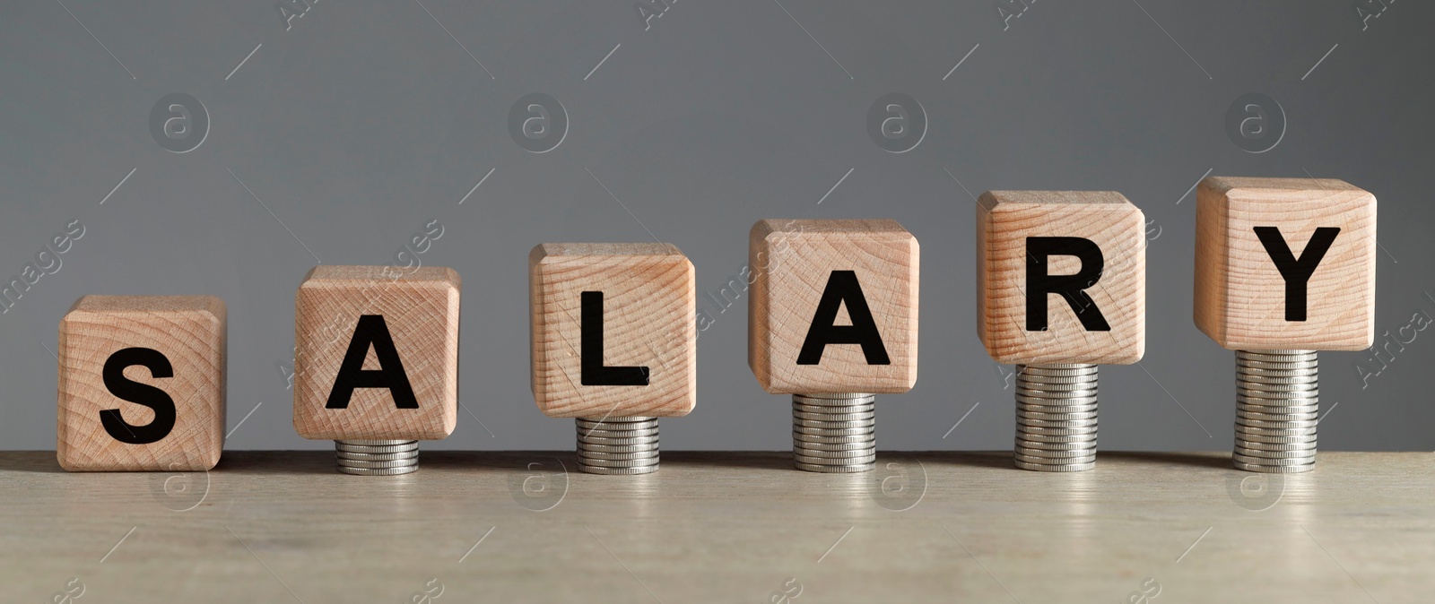 Photo of Word Salary made of cubes and stacked coins on light wooden table against grey background, closeup