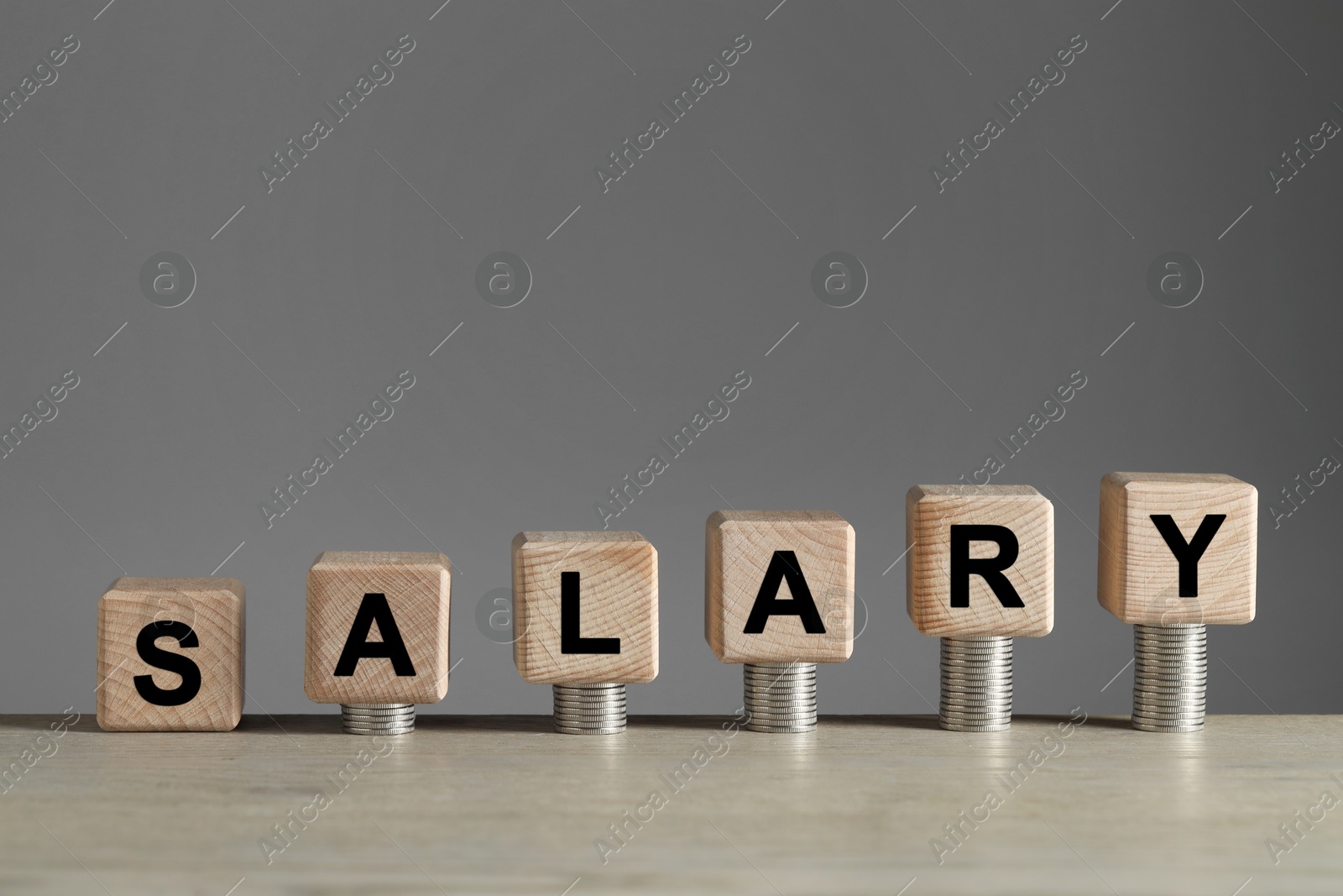 Photo of Word Salary made of cubes and stacked coins on light wooden table against grey background