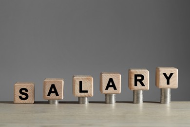 Word Salary made of cubes and stacked coins on light wooden table against grey background