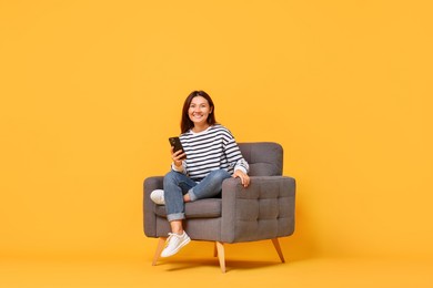 Photo of Smiling woman with smartphone sitting in armchair on yellow background